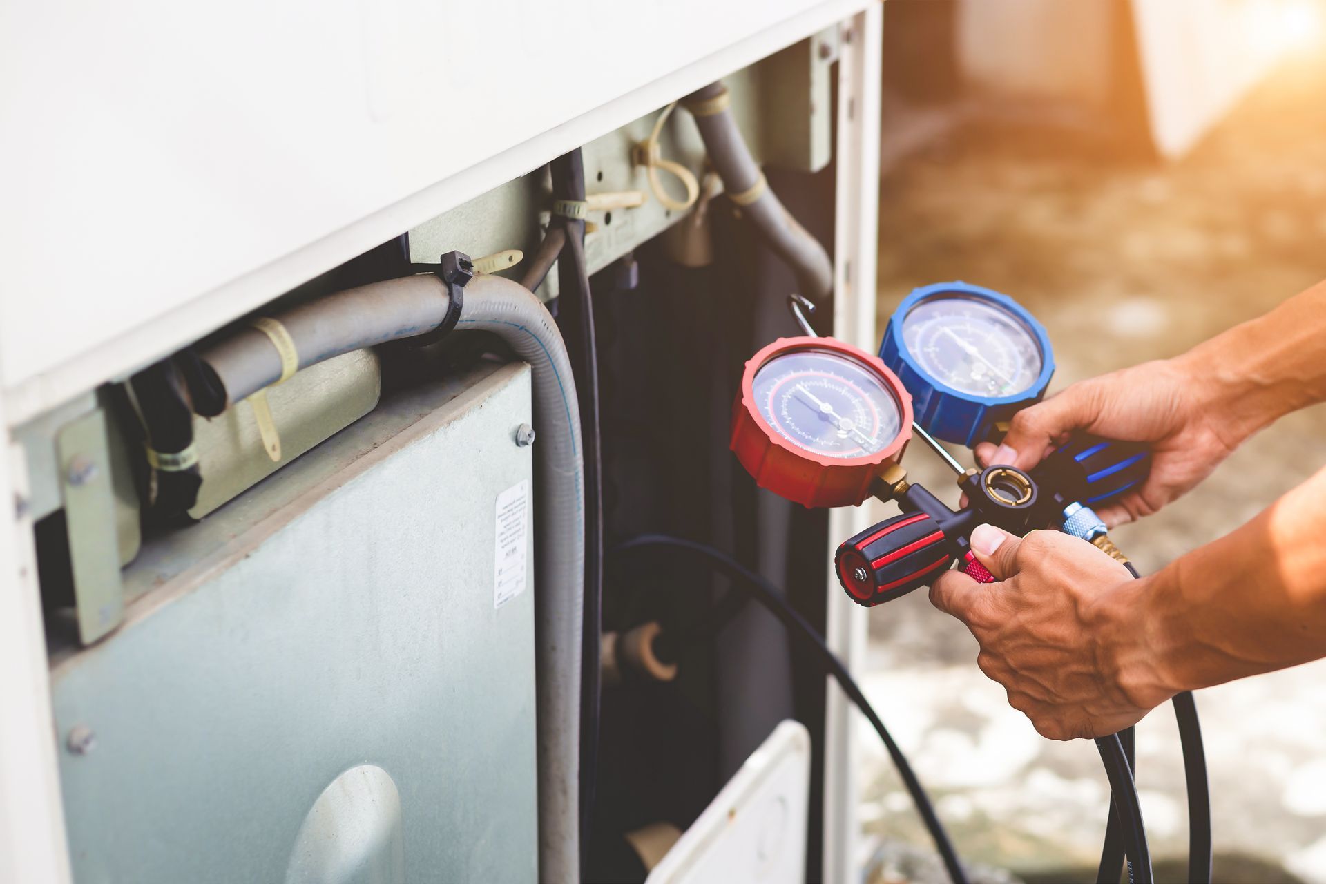 Technician checking HVAC unit pressure with a dual gauge manifold outdoors.