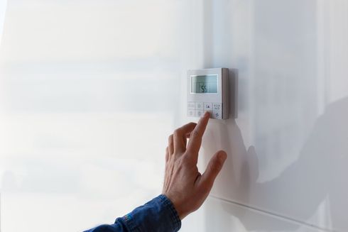 Hand adjusting a wall-mounted thermostat on a white wall.