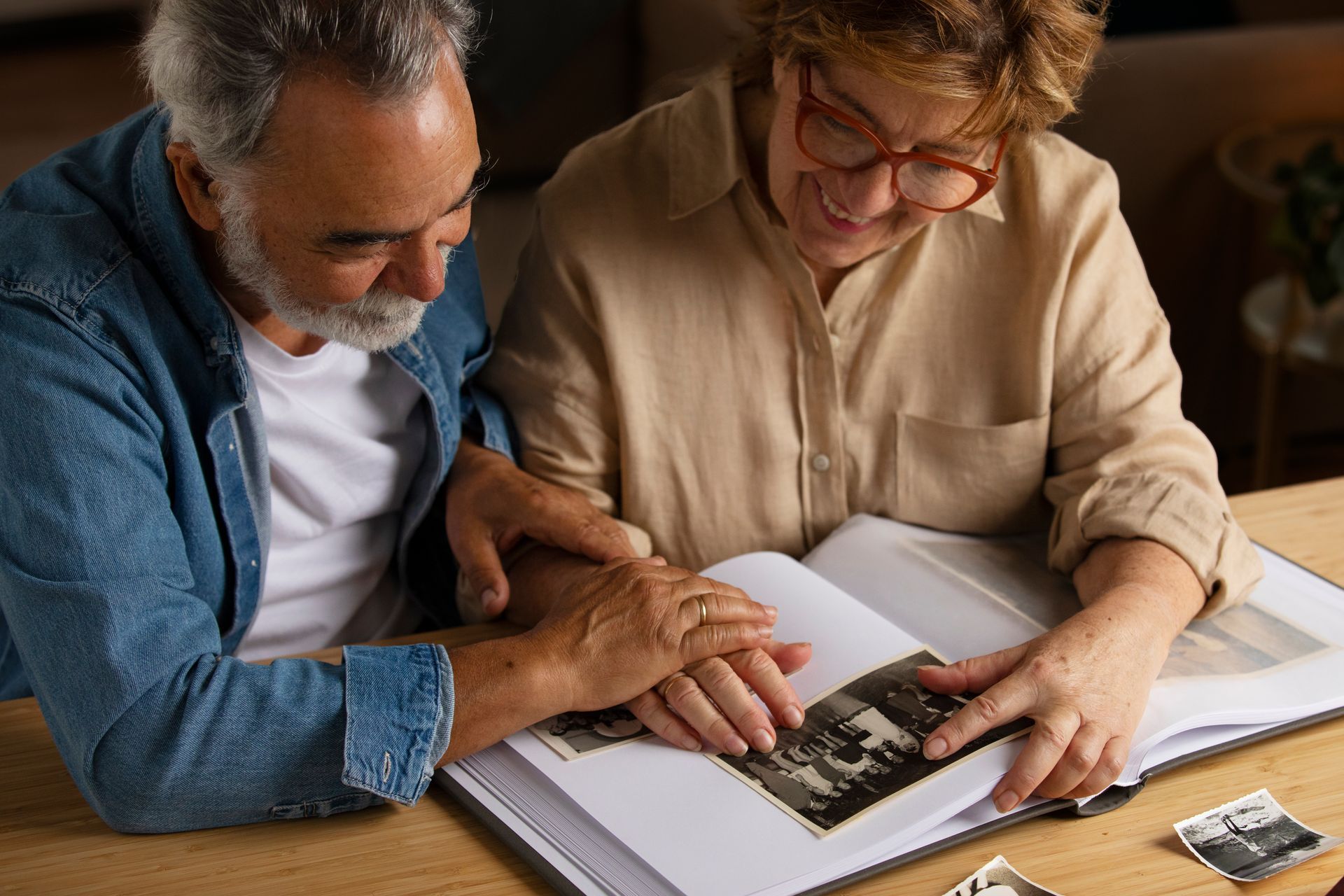 Senior couple looking at a photo album, smiling. Indoors, wooden table.