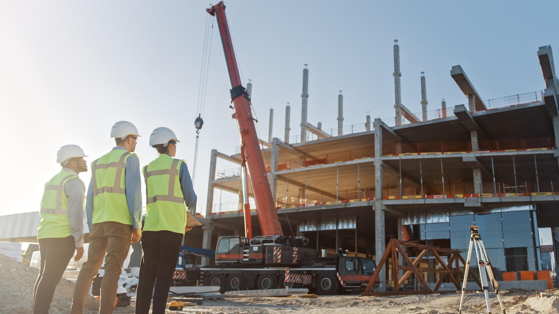 Construction workers in vests and hardhats survey a building site with a crane.