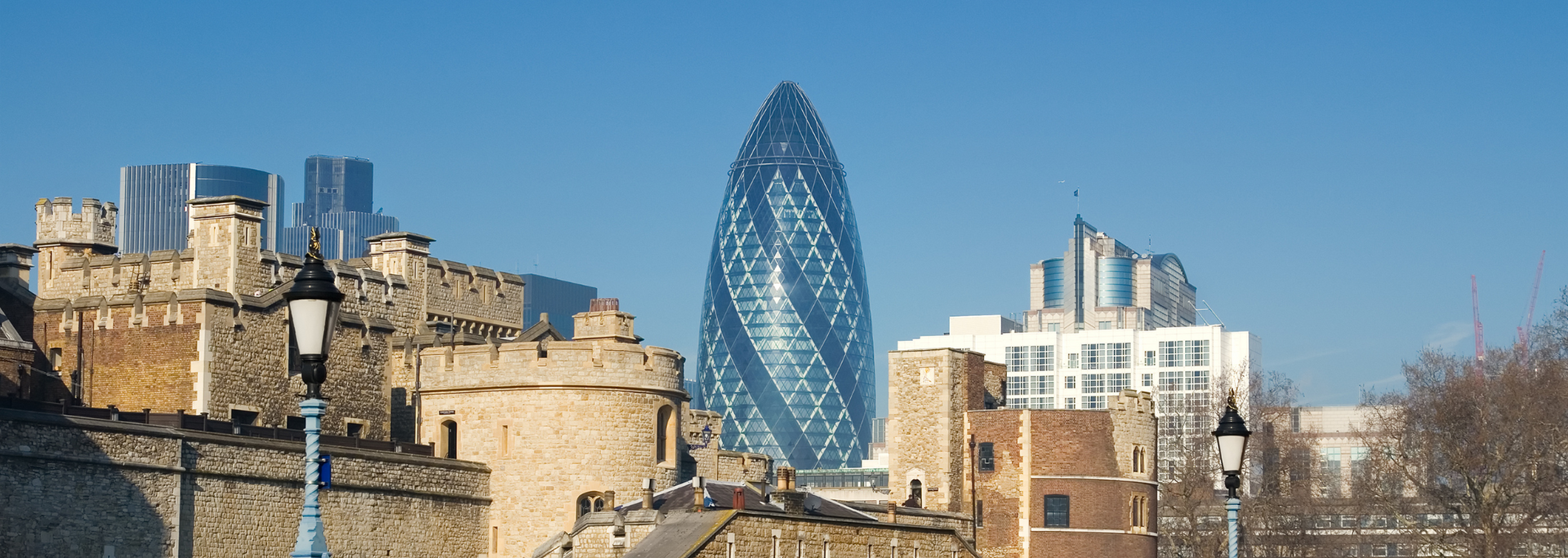 The Gherkin skyscraper and Tower of London against a clear blue sky.