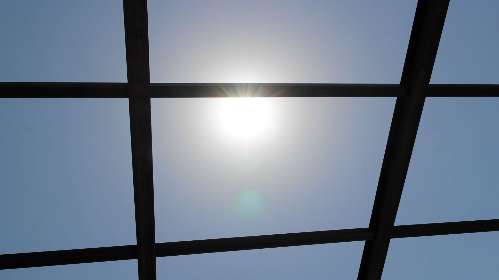 Sun shining through a dark grid against a blue sky.