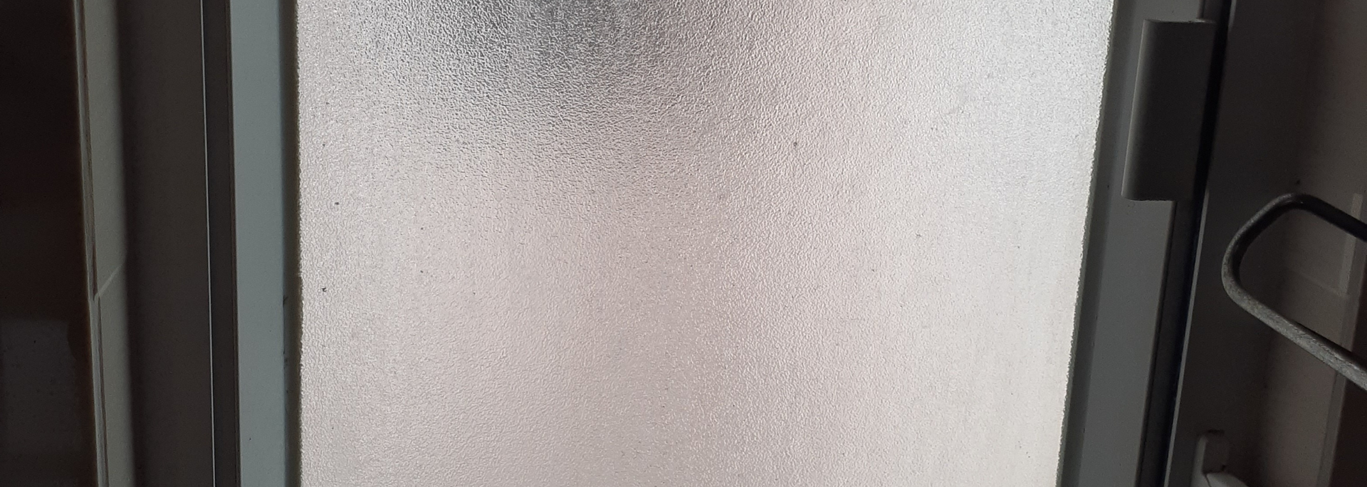 Frosted glass shower door in a dark-colored frame. A black handle is partially visible.
