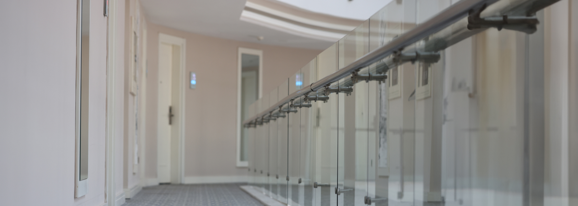A hallway with a glass railing and doors on the left, and a long walkway.