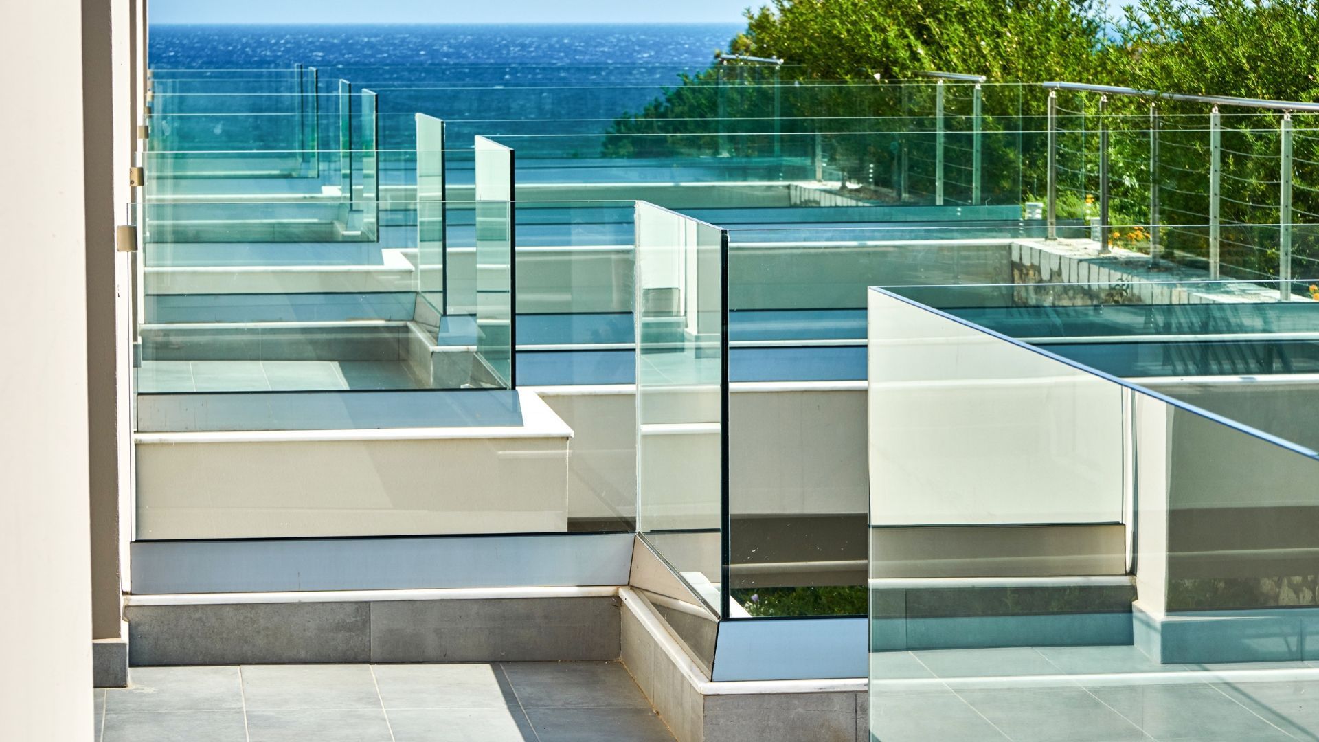 Staircase with glass railings leading to a view of the ocean. White and gray stone construction.