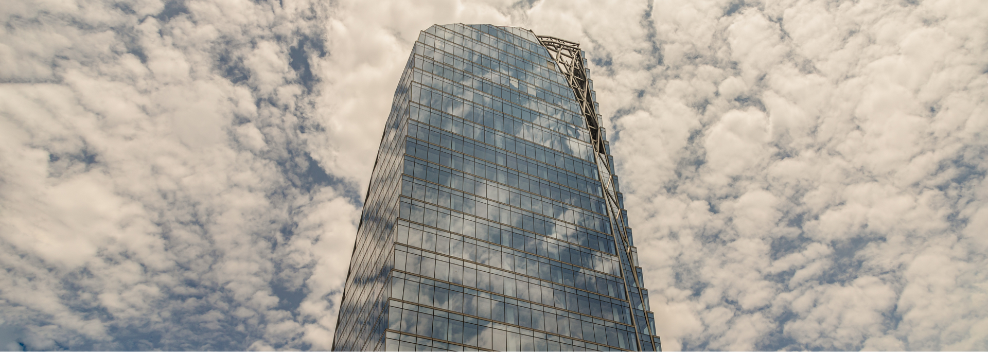 A tall glass skyscraper against a cloudy sky.