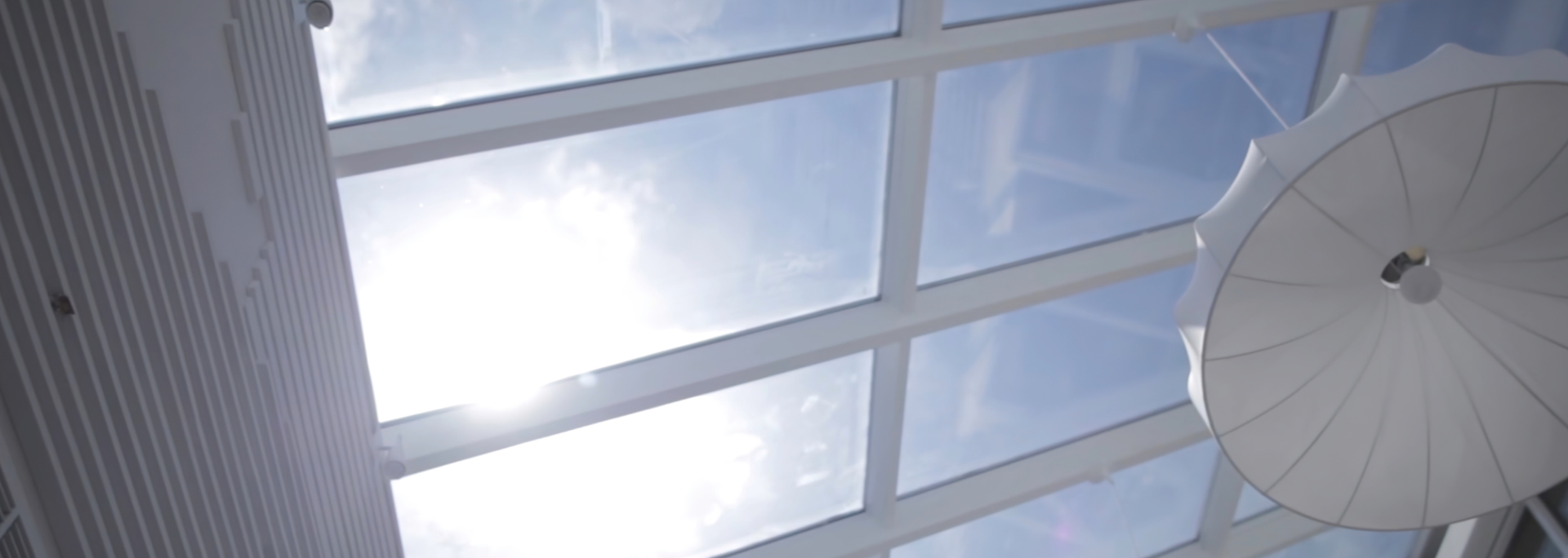 Skylight ceiling with a sunny blue sky peeking through, and a white, umbrella-like structure hanging.