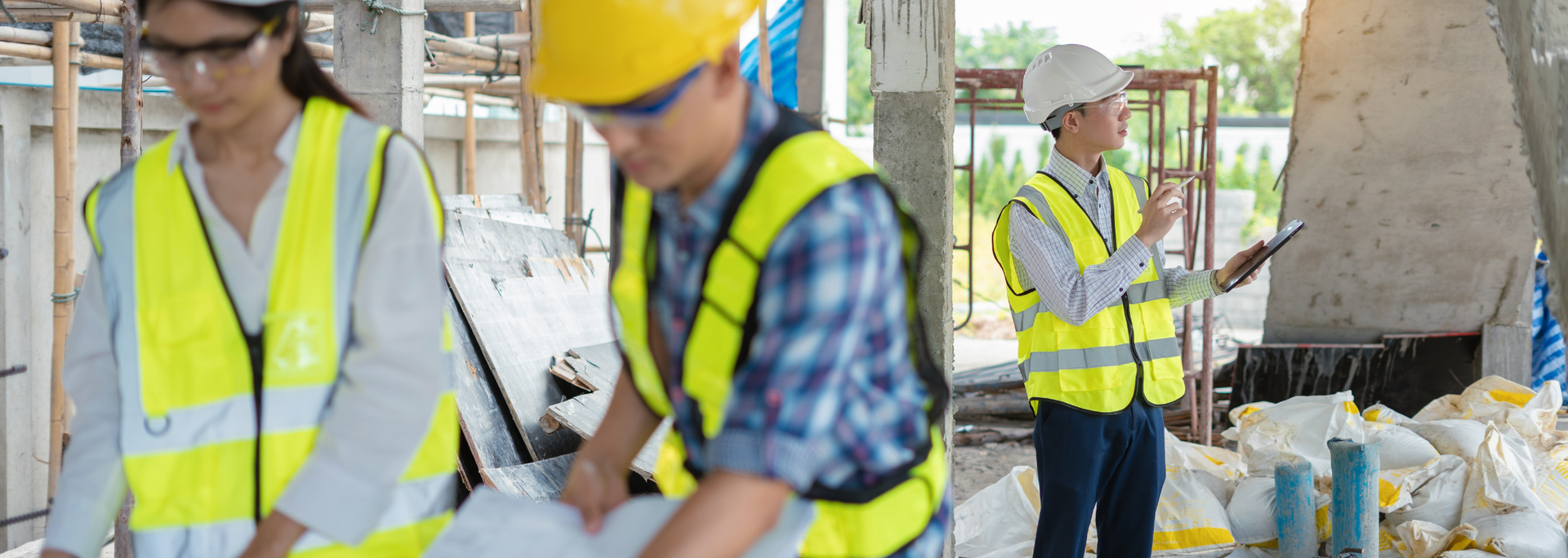 Construction workers in safety vests, helmets, and glasses, reviewing blueprints on a construction site.