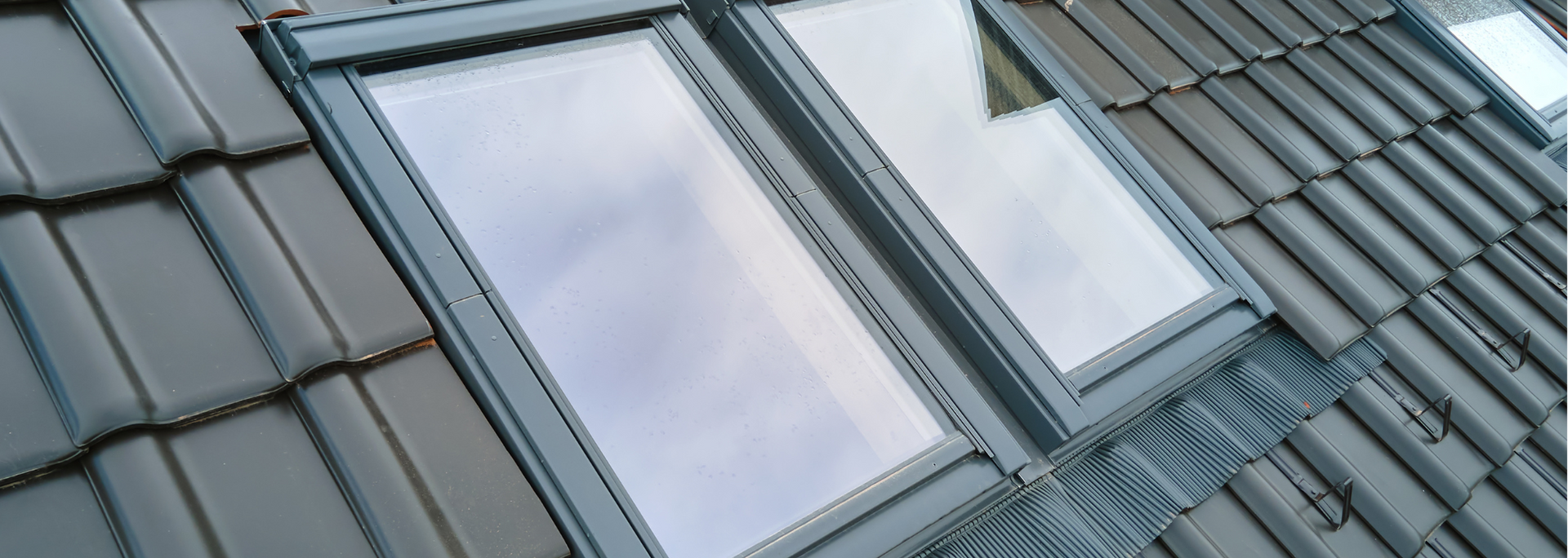 Skylights on a tiled roof, reflecting the sky and surrounding environment.