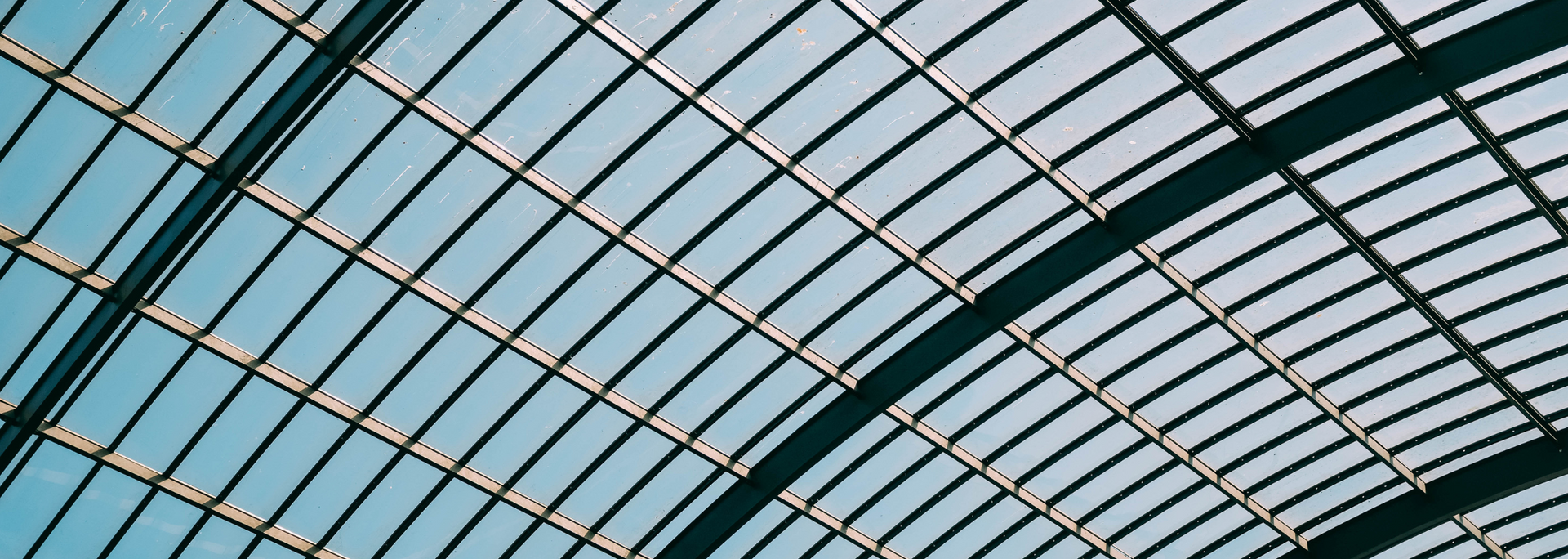 A glass ceiling with a grid pattern, casting shadows against a blue sky.