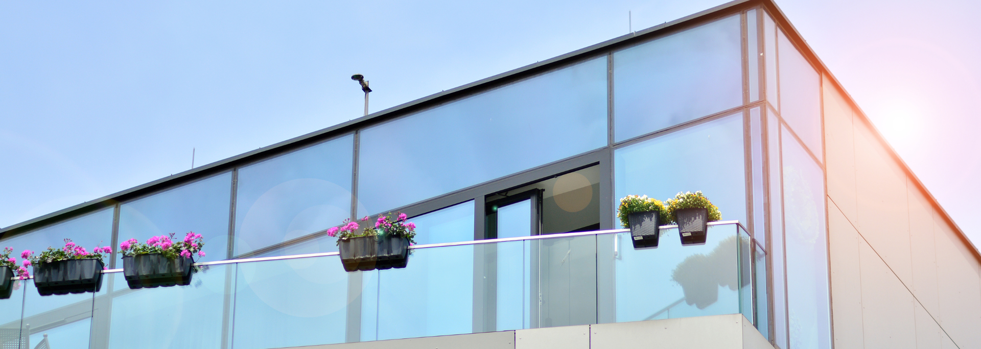 Modern building with glass facade and balcony with flower boxes.