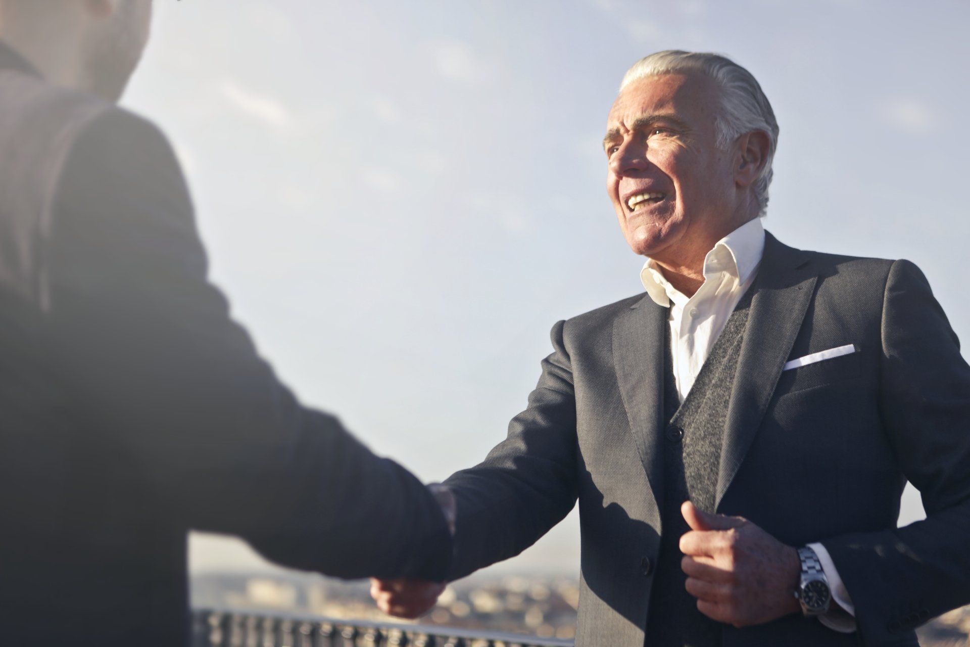Two men in suits shaking hands outdoors; one smiles.
