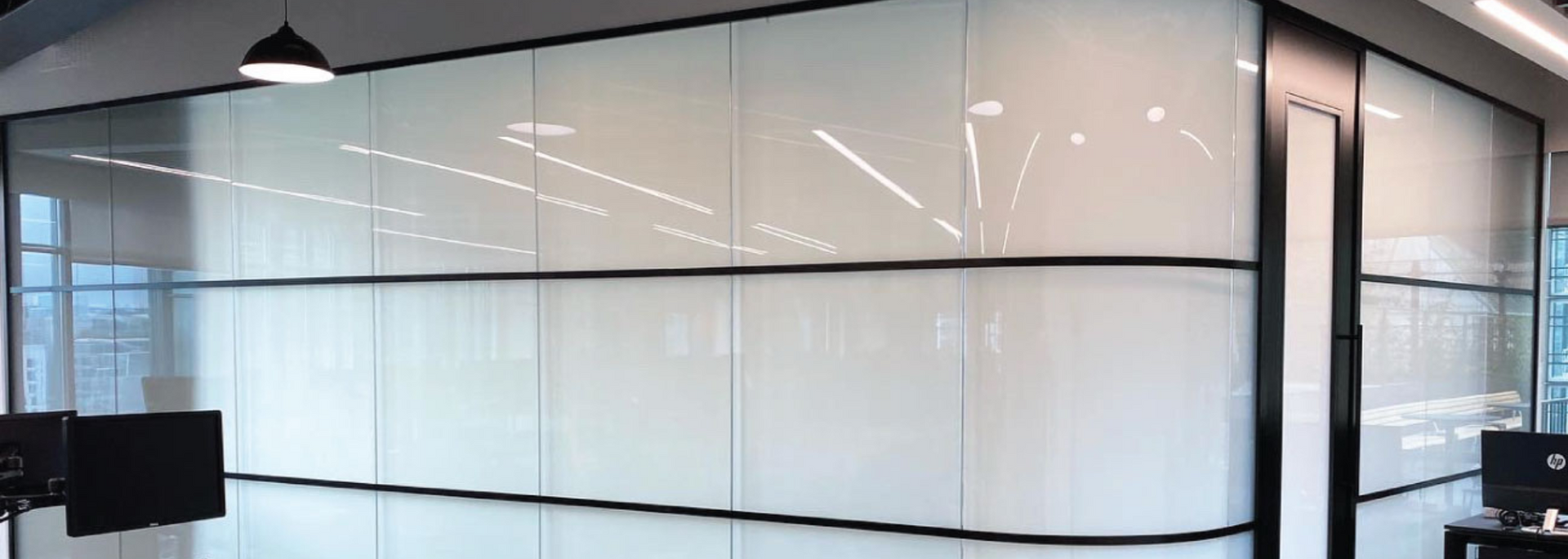 Office space with frosted glass walls and black frames. A door is visible.
