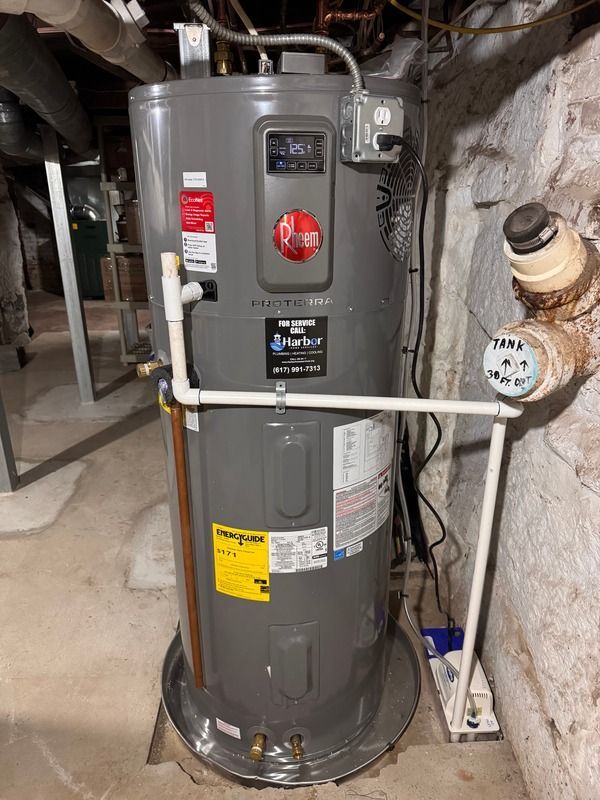 Gray water heater in a basement with pipes, valves, and utility labels.