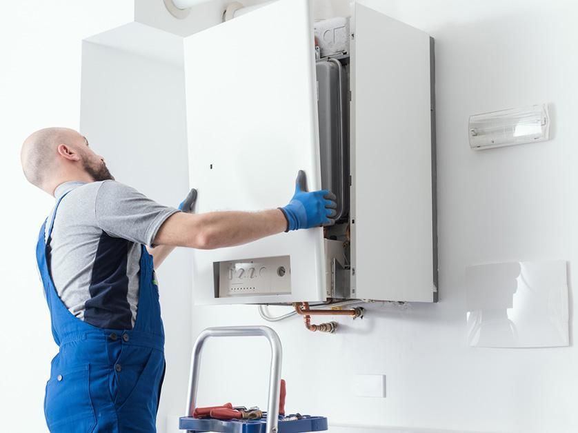 Technician in blue coveralls installing a white wall-mounted boiler.
