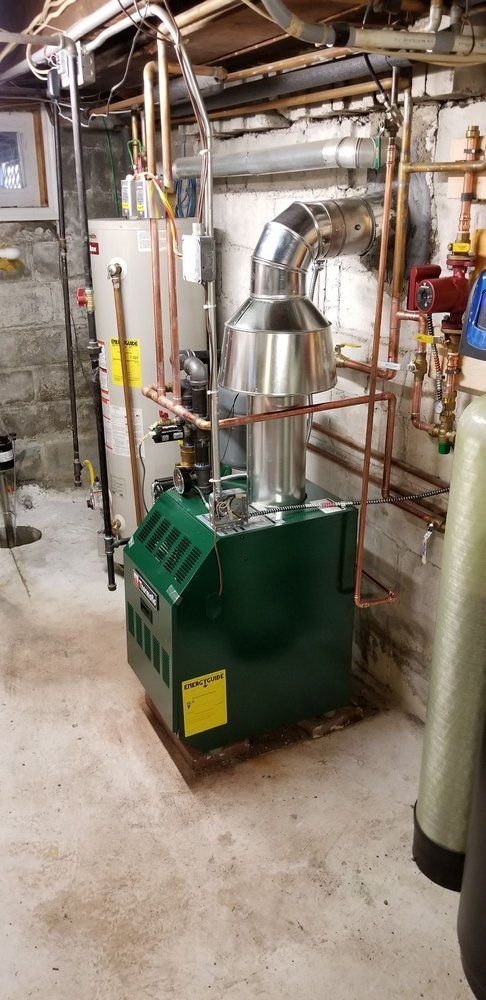A green boiler is sitting in a basement next to a water heater.