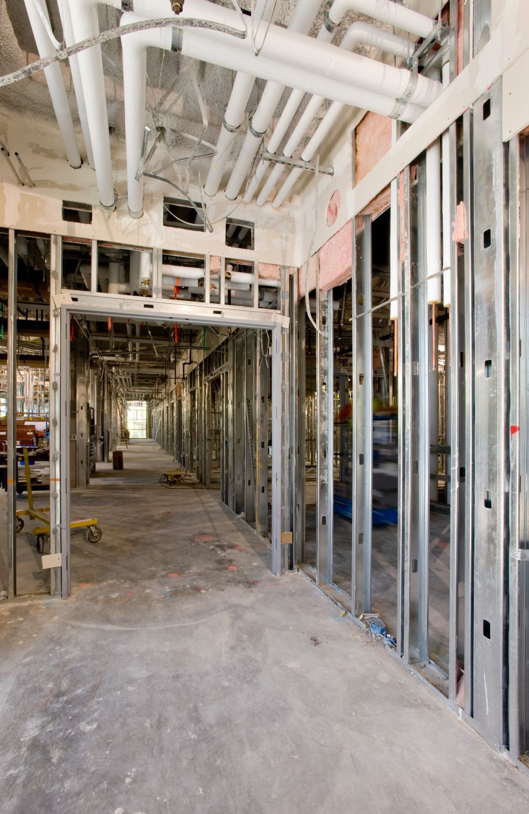 A long hallway in a building under construction with pipes hanging from the ceiling.