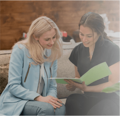 Two women are sitting on a couch looking at a book.