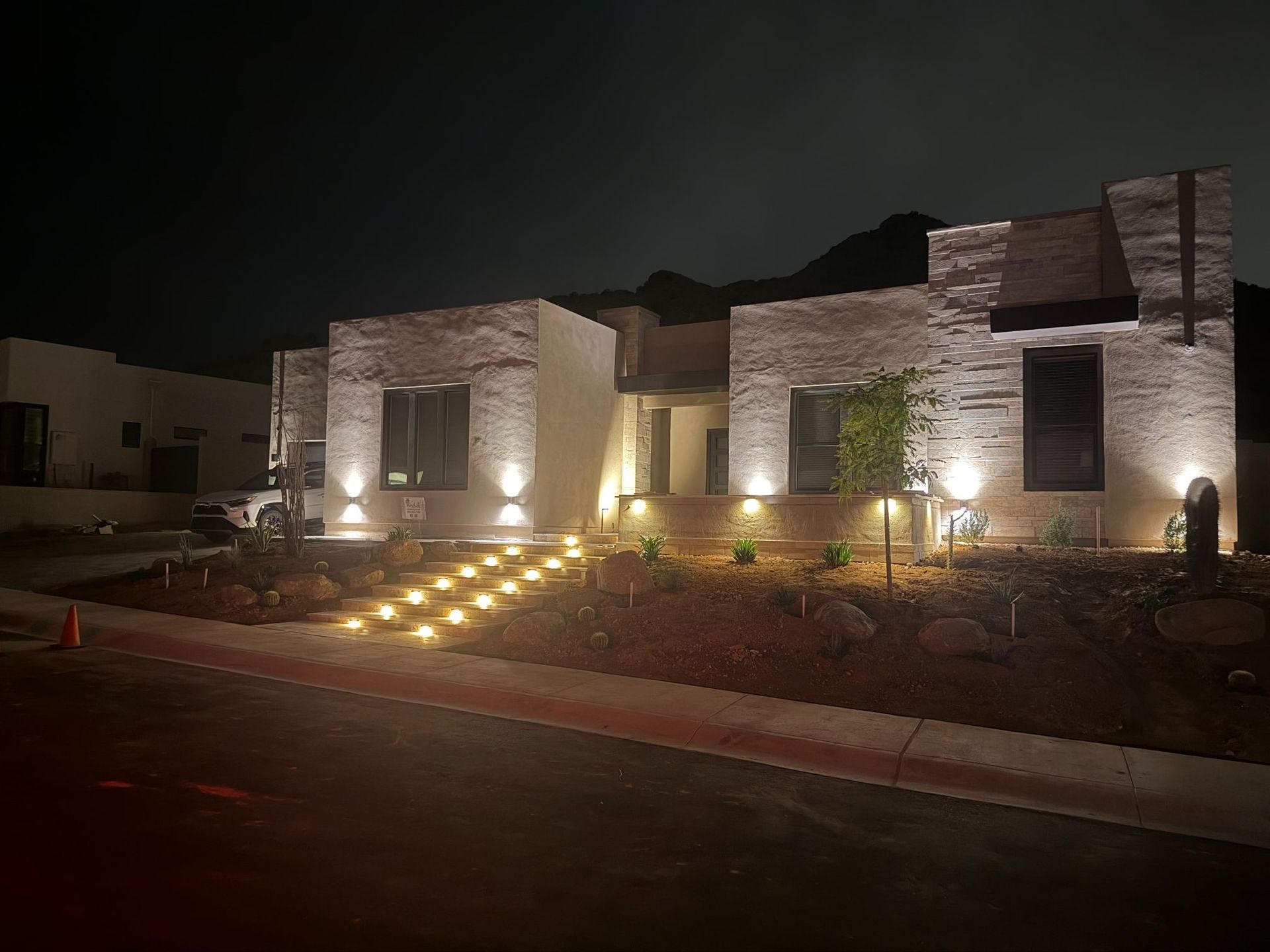 Modern stone house exterior at night with illuminated walkway and landscaped front yard