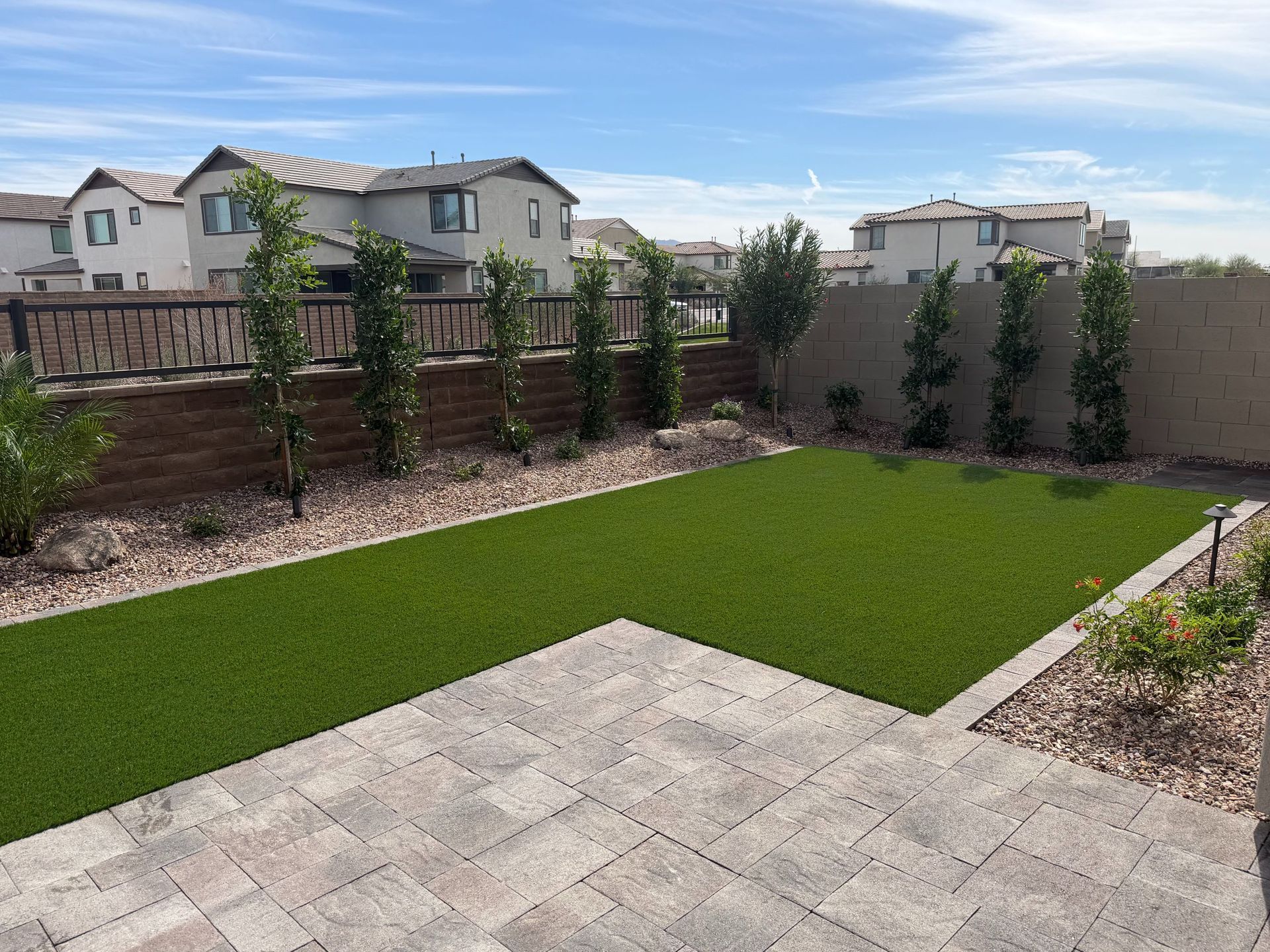 Backyard patio with artificial grass, stone paving, and a fenced garden under a blue sky