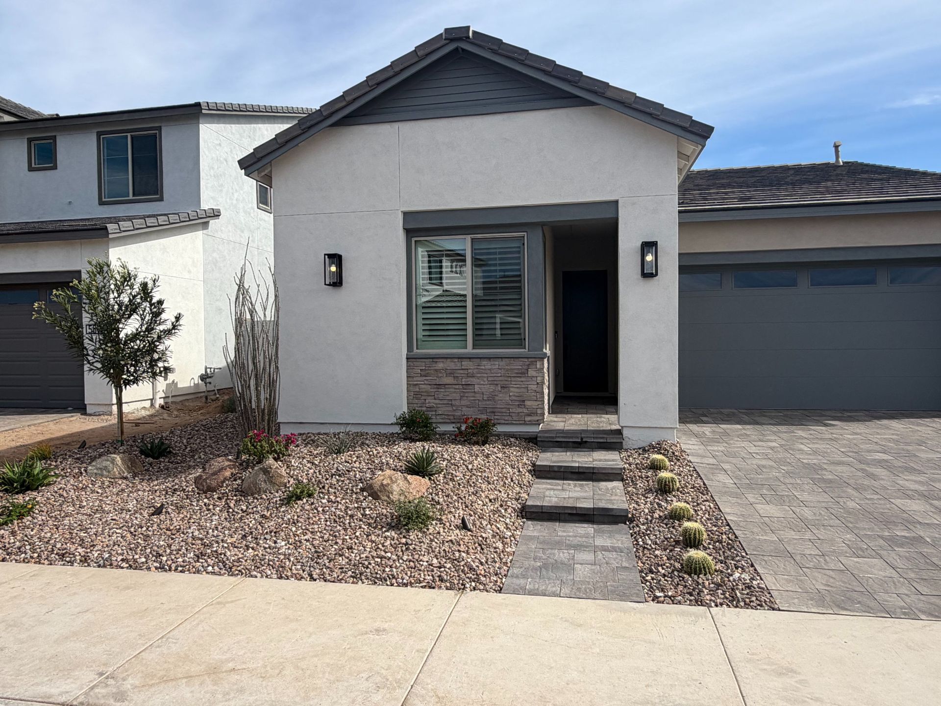 Small white stucco house with a front walkway, desert landscaping, and a closed garage.