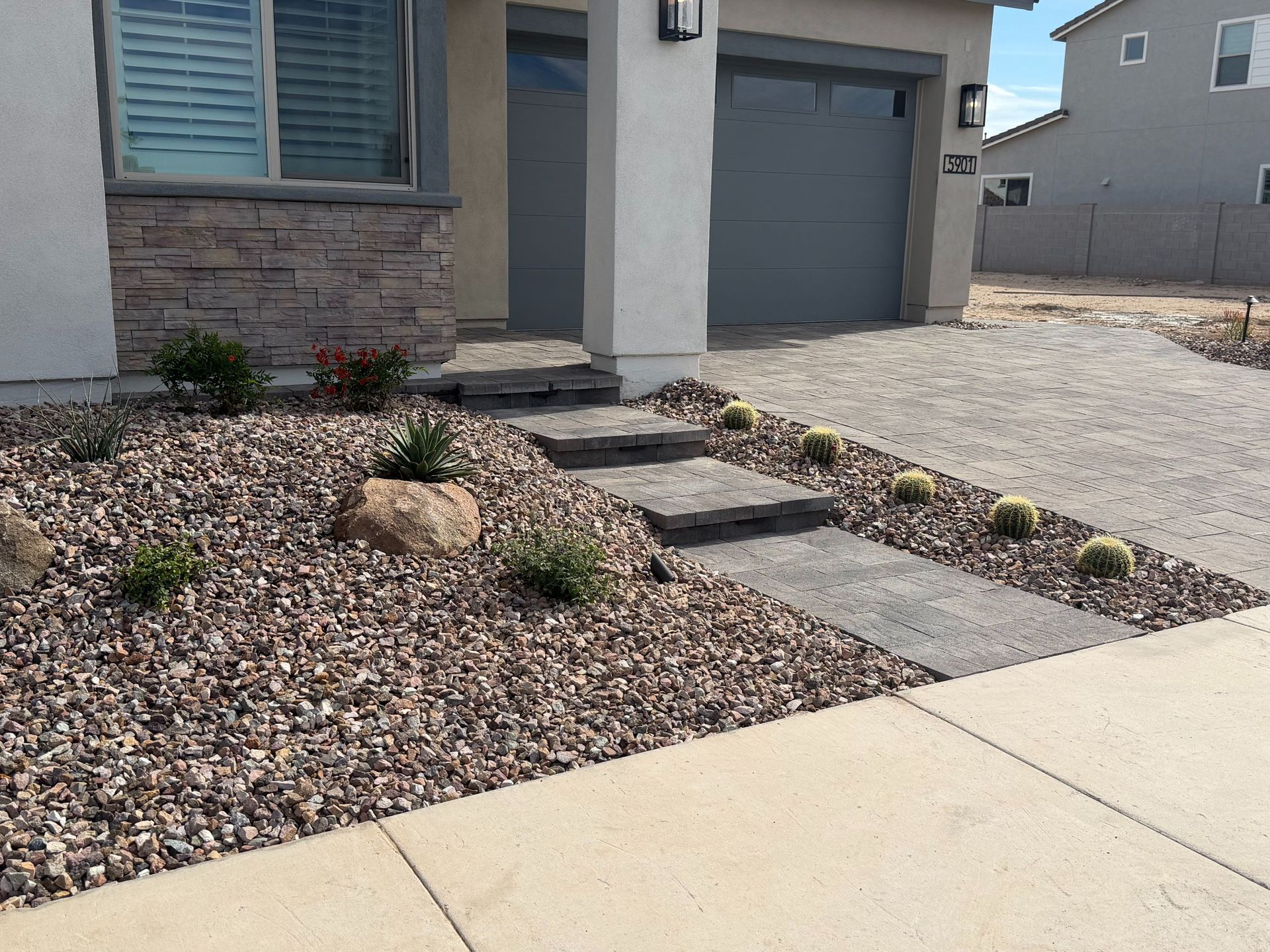 Front yard with desert landscaping, stone walkway, and garage beside a concrete sidewalk.