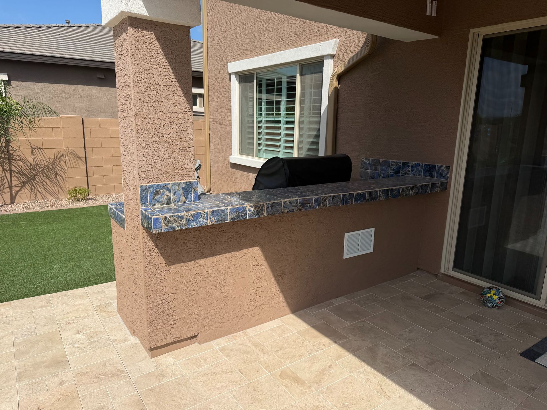 Outdoor patio with built-in stone grill counter beside a sliding glass door and lawn.