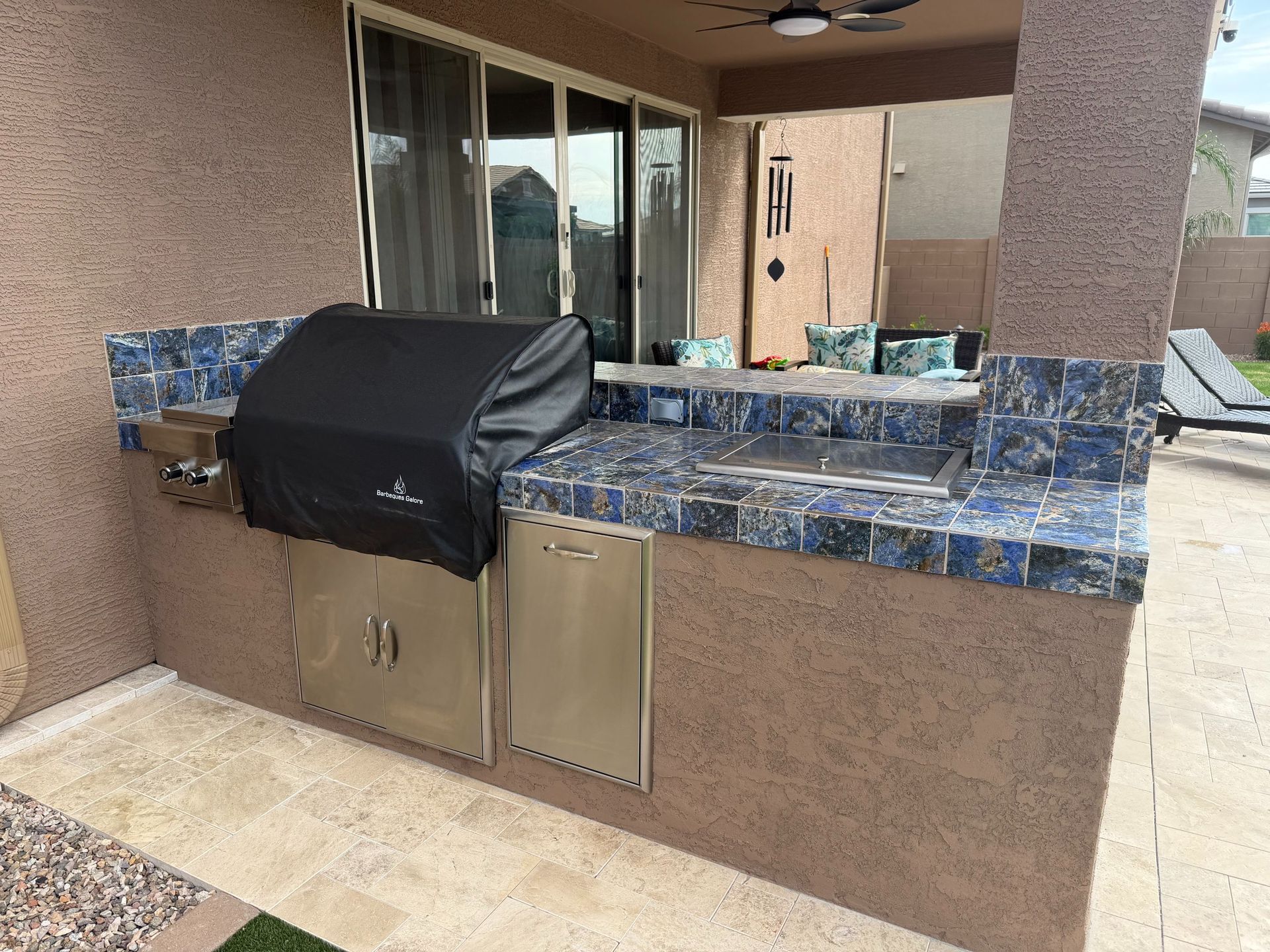 Outdoor patio with built-in grill, blue tile countertop, and sink beside a stucco wall