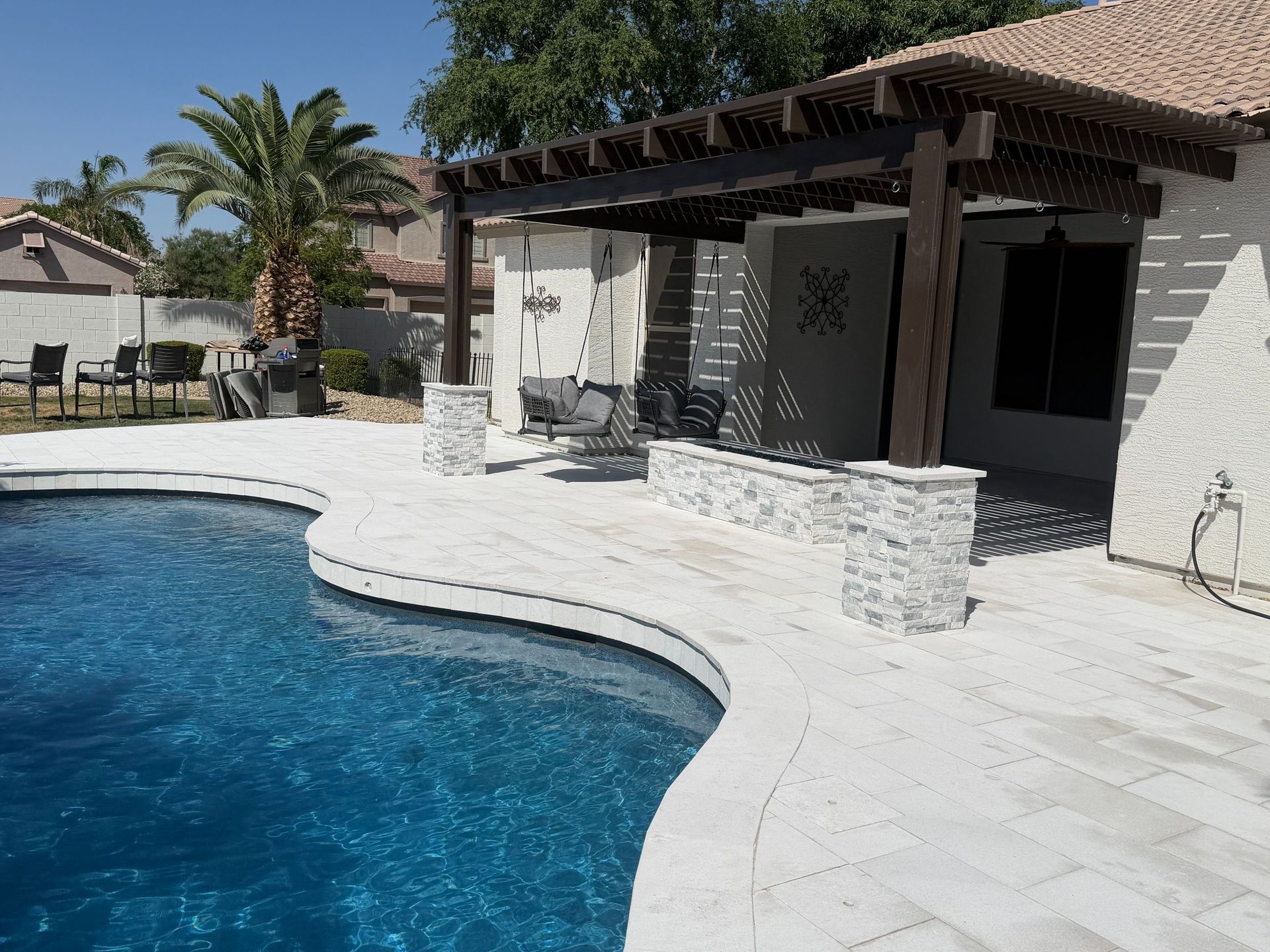 Backyard pool with curved blue water, white patio, and a covered outdoor seating area.