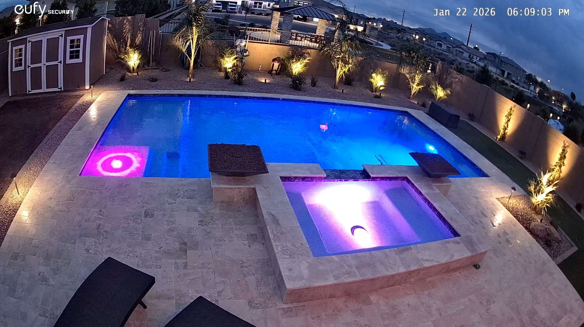 Modern backyard at night with lit blue pool, pink hot tubs, and surrounding patio lighting