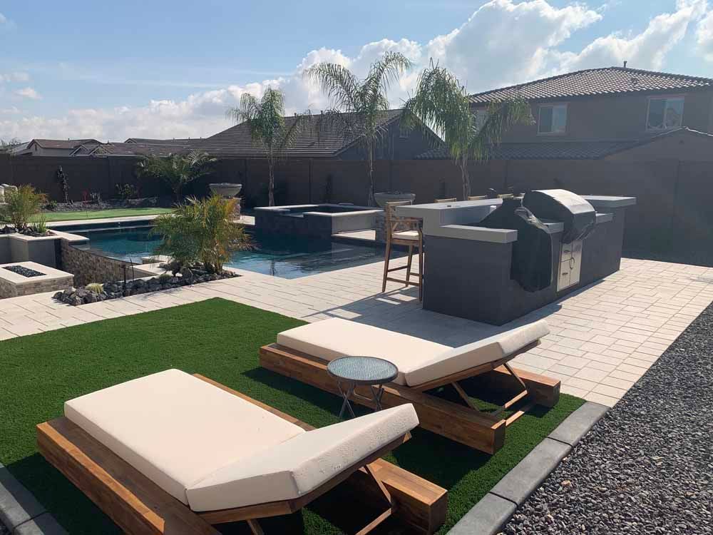 Backyard with pool, outdoor kitchen, lounge chairs, and palm trees. Sunny day.