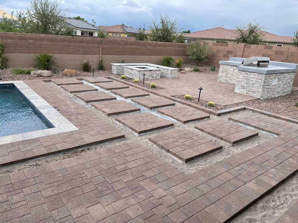 Backyard patio with pool, stone pavers, fire pit, and grill. Brown tones dominate the scene.