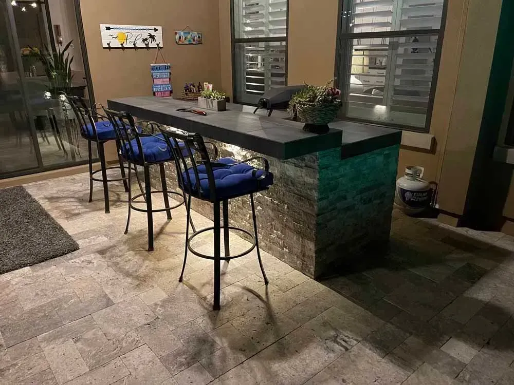 Outdoor bar with a stone base, gray countertop, and bar stools.
