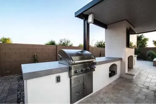 Stone outdoor pavilion with a dark wooden roof, built-in grill, and bench seating.