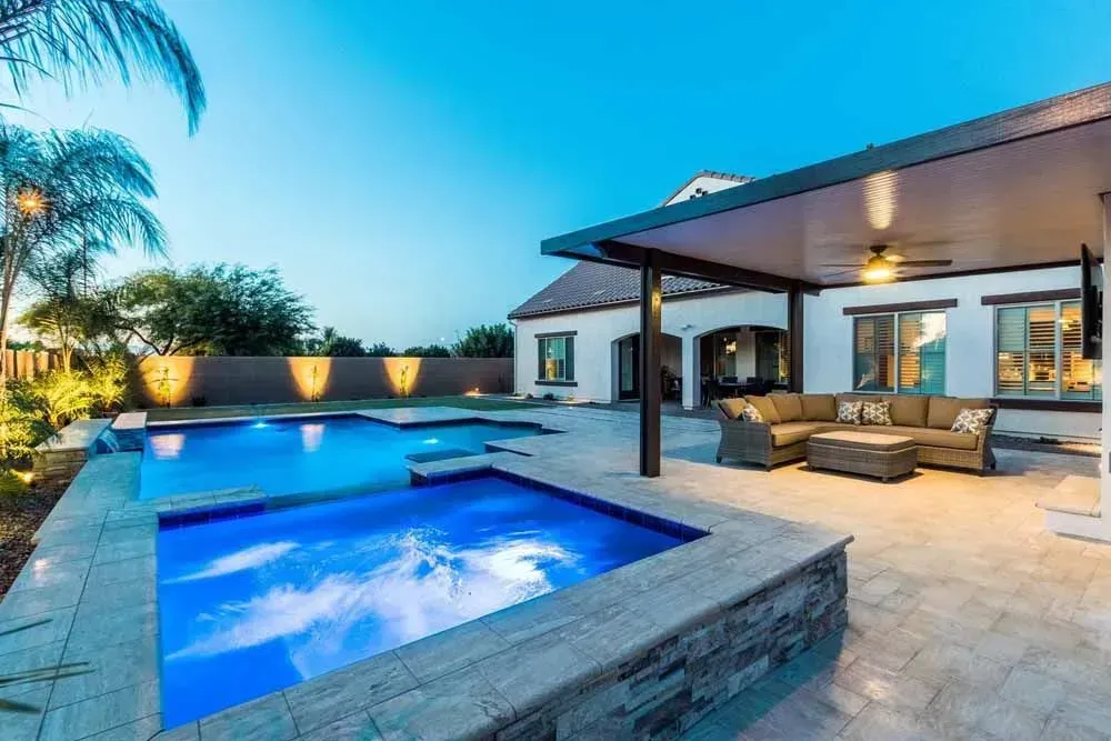 Backyard with pool, spa, patio, and seating area illuminated at dusk.