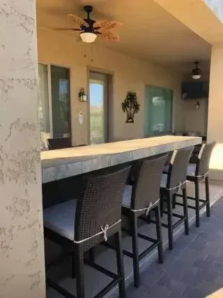 Outdoor bar with six wicker bar stools, under a covered patio with a ceiling fan.