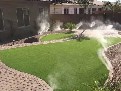 Lawn with misting system in a backyard; green grass, stone path, and shrubs.
