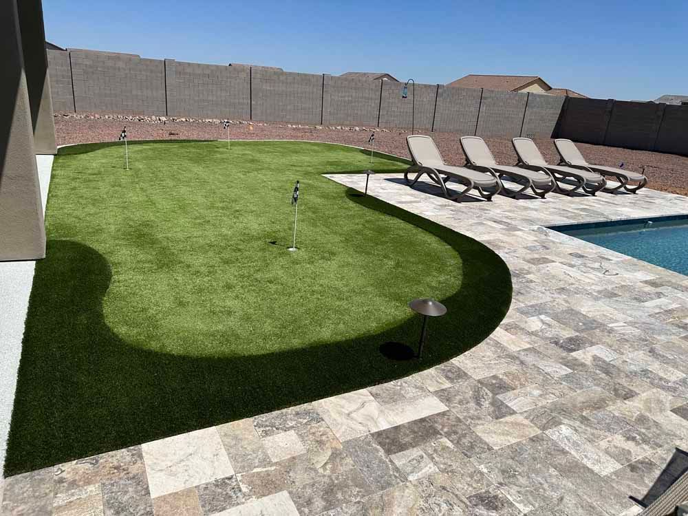 Backyard with putting green, pool, lounge chairs, and high stone wall.