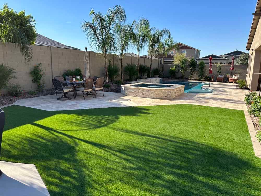 Backyard with pool, hot tub, dining set, and artificial grass under a sunny sky.