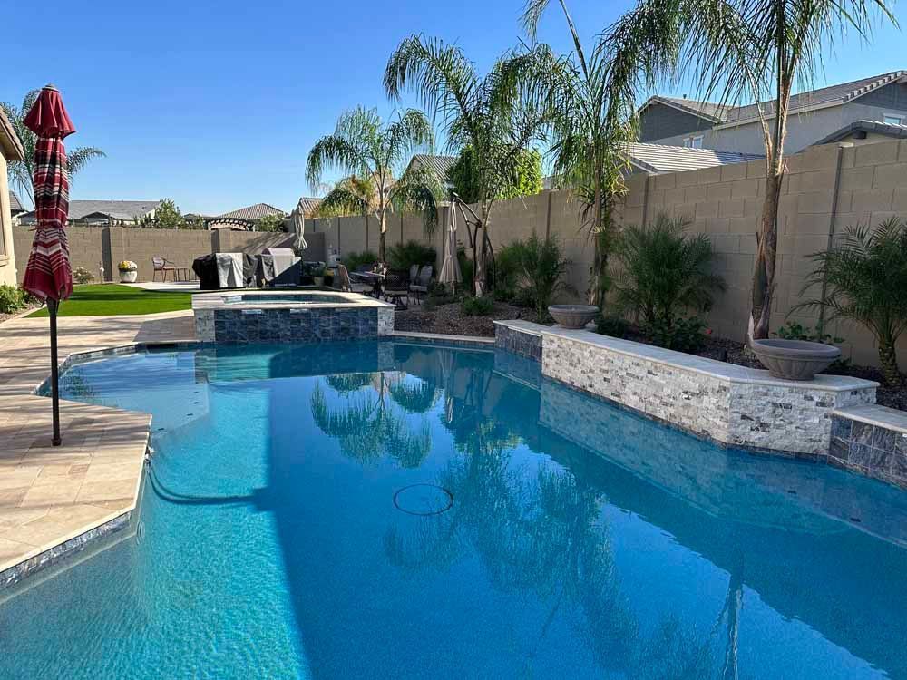 Swimming pool with blue water, surrounded by patio and palm trees under a sunny sky.