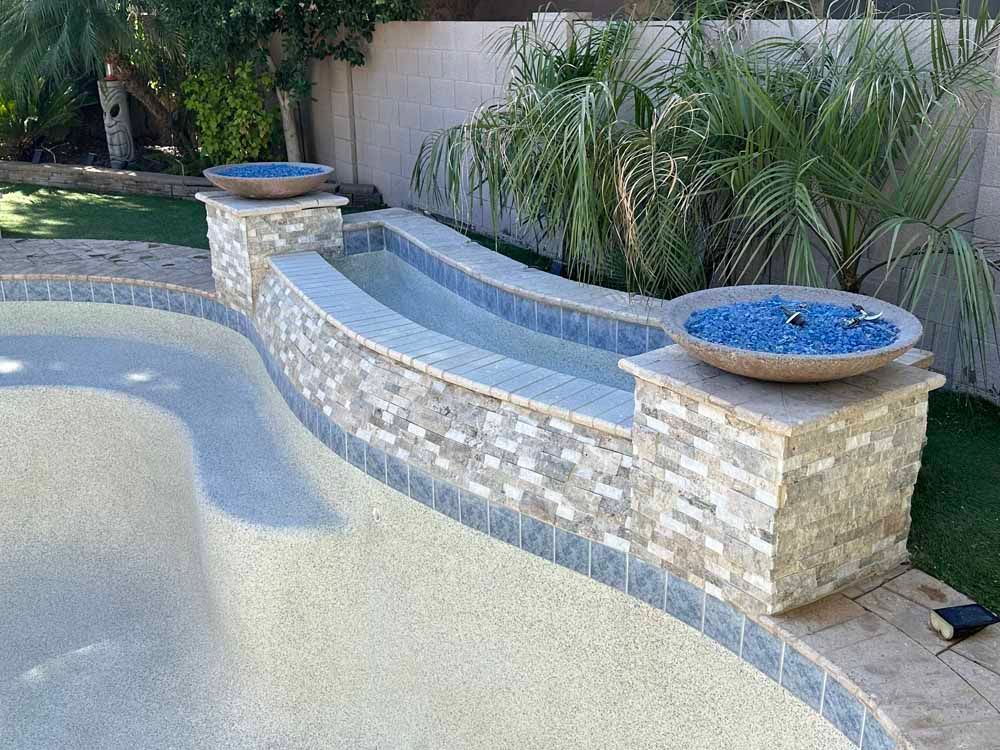 Swimming pool with a raised water feature, stone facade, and blue glass fire pits.
