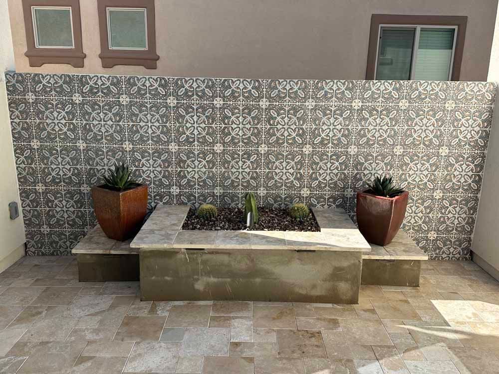 Patio with tiled wall, built-in planter with cacti, two potted plants on the sides, and stone flooring.