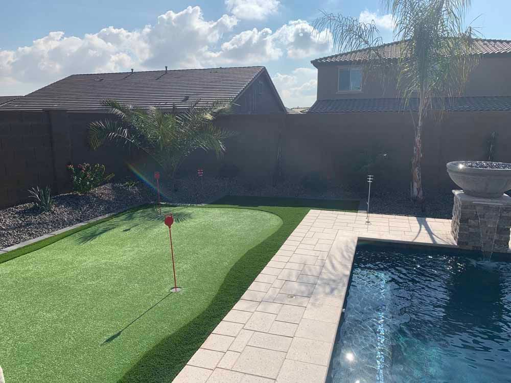 Backyard with putting green, pool, and home. Green grass, blue water, and brown walls.
