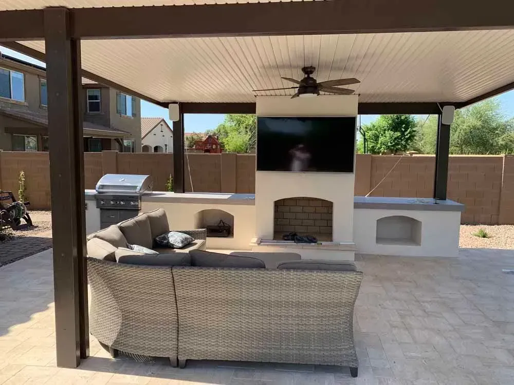 Outdoor patio with kitchen, fireplace, TV, and sectional sofa under a covered pergola.