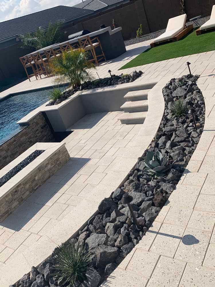 A modern backyard with a pool, patio, and rock garden. Artificial grass, steps, and outdoor bar.