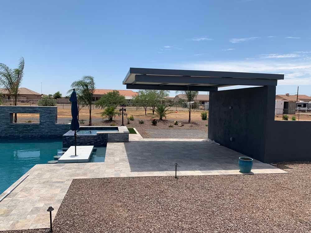 Backyard pool with patio, hot tub, and modern dark gray shade structure on sunny day.