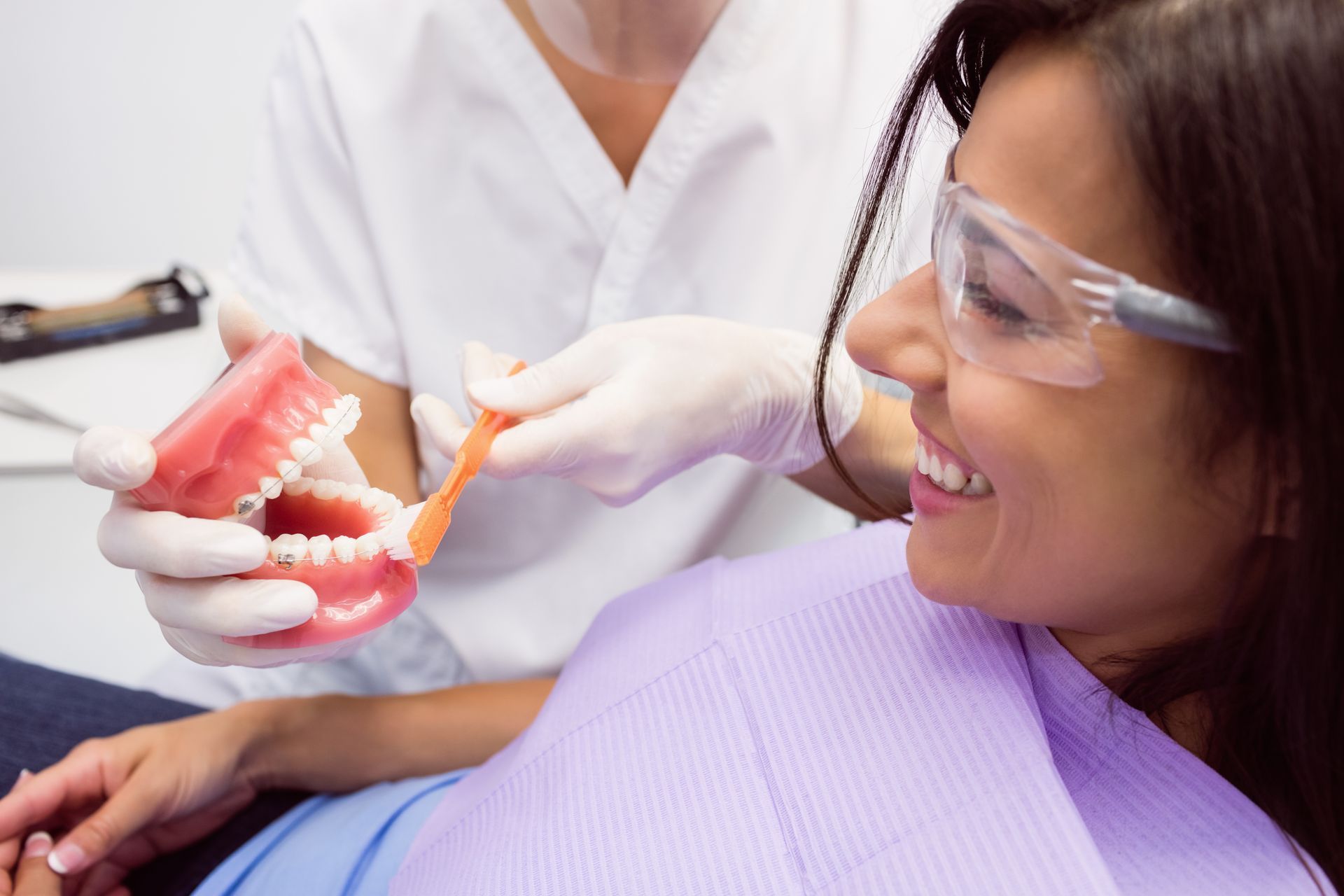 A woman is sitting in a dental chair while a dentist cleans her teeth with a toothbrush.
