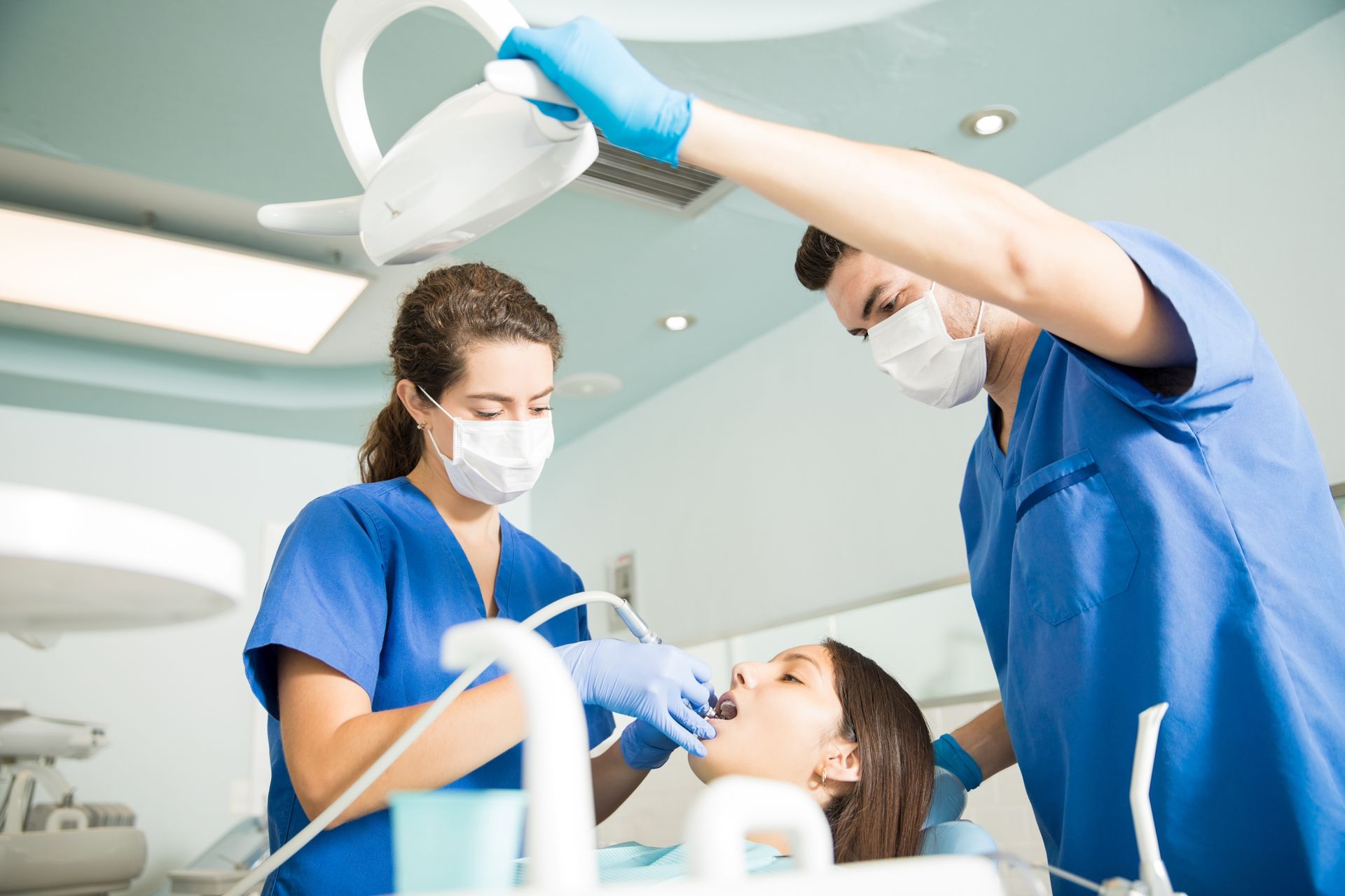 A woman is getting her teeth examined by two dentists in a dental office.