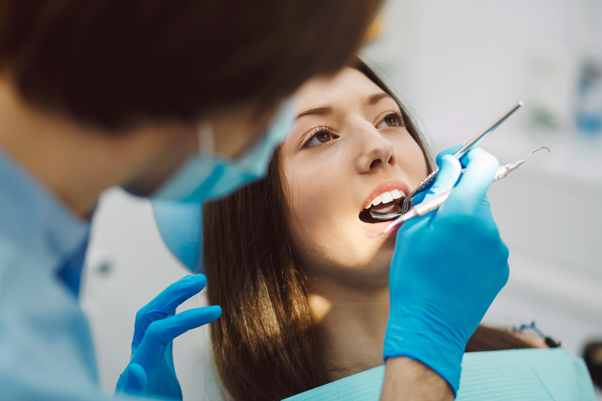 A woman is sitting in a dental chair while a dentist examines her teeth.