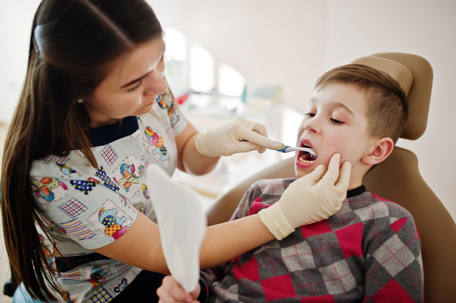 A young boy is sitting in a dental chair while a dentist examines his teeth.